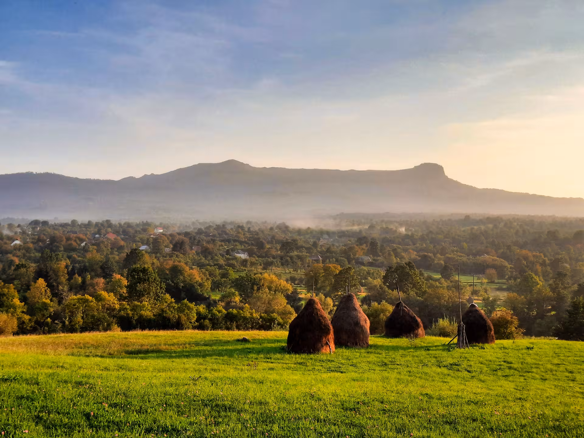 Misty Maramures countryside with haystacks on green hillside and mountains in background
