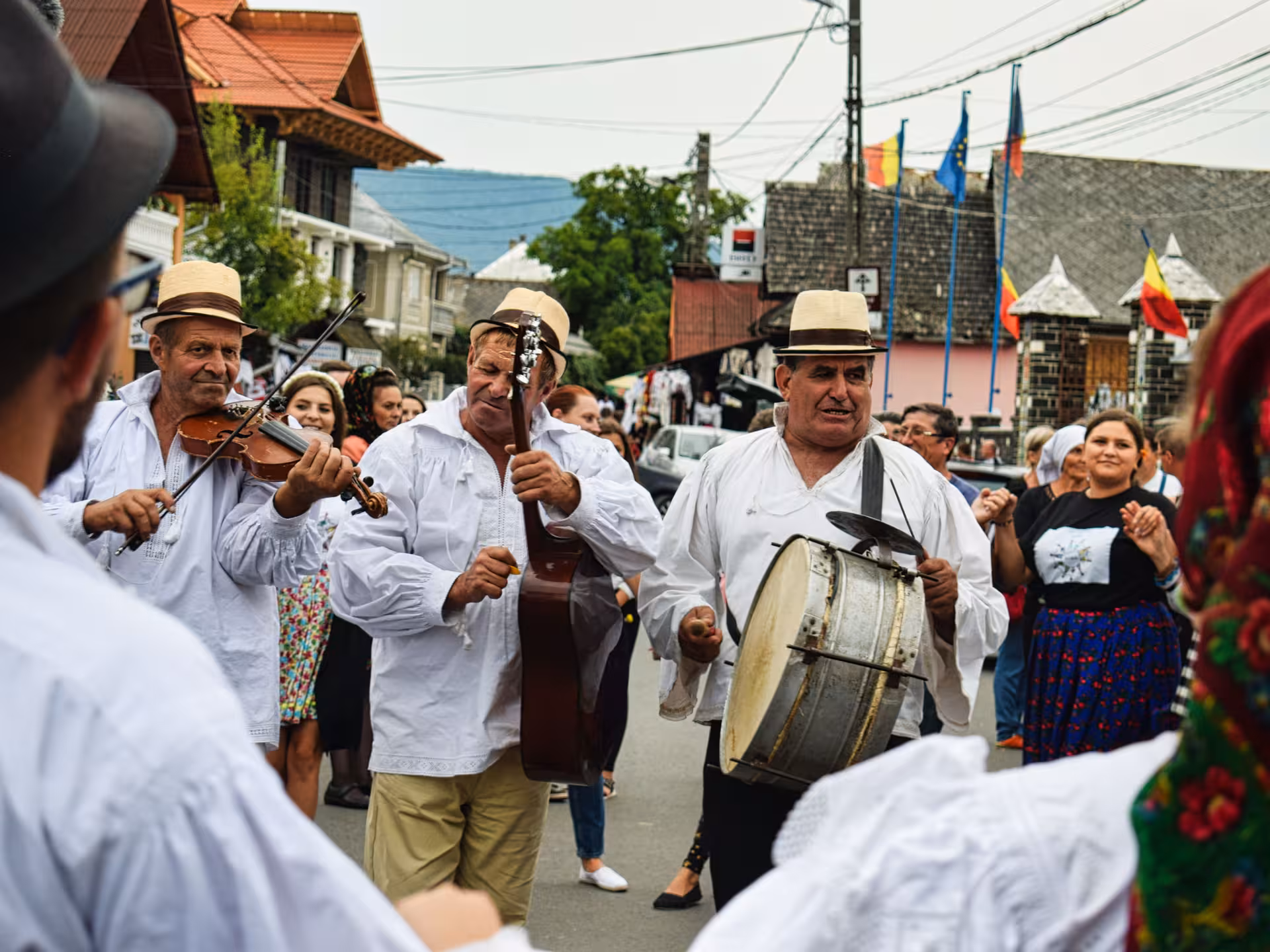 Traditional Maramures folk musicians in white costumes playing violin and drum at a lively village street festival