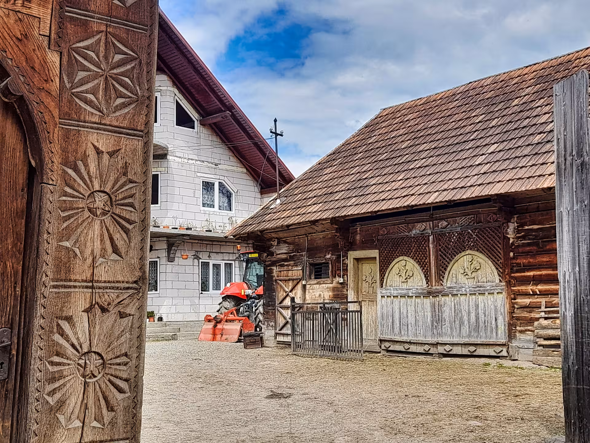 Traditional carved wooden gate leading to a Maramures farmstead with log barn and red tractor in Romania