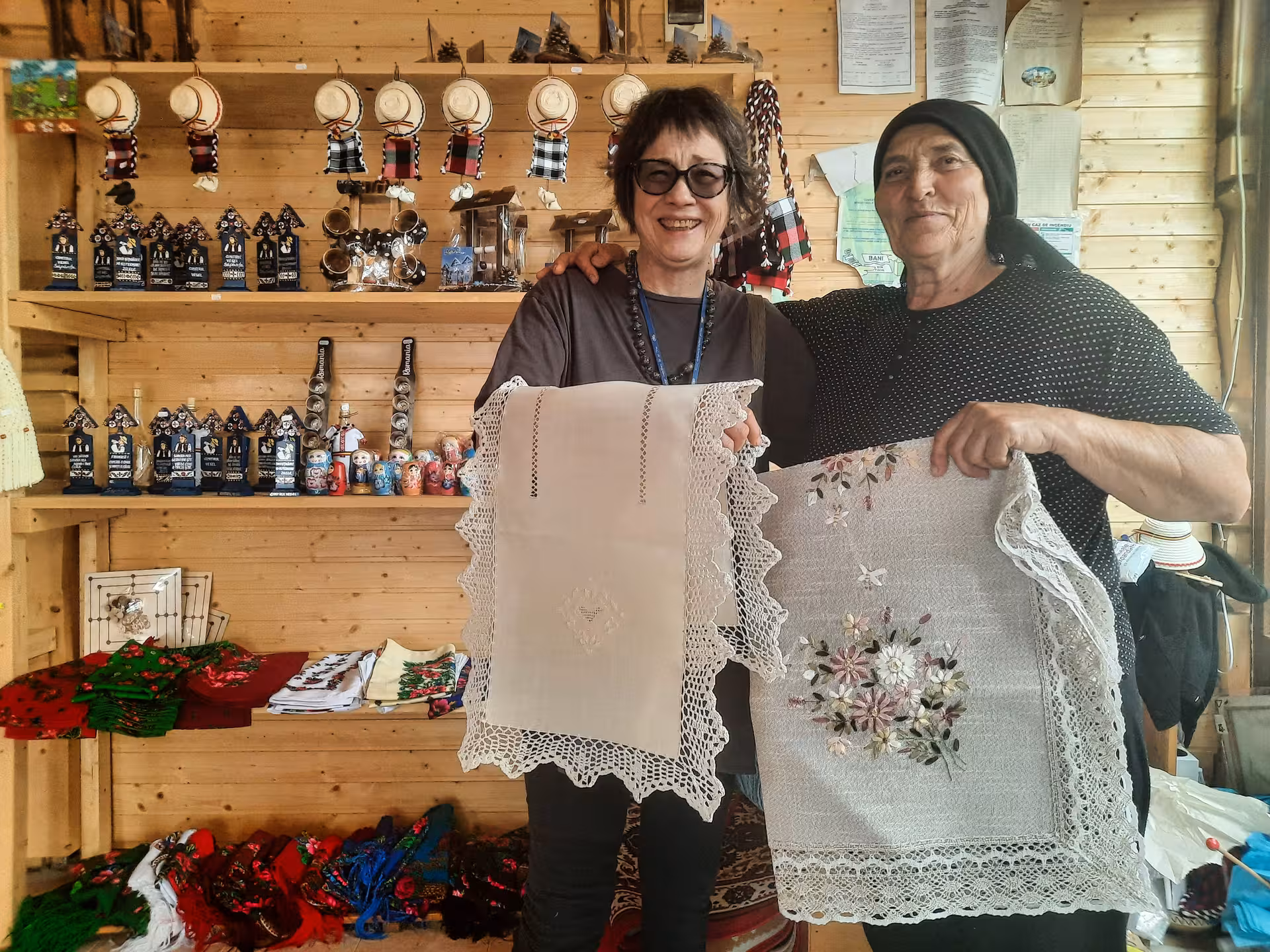 Local artisan and tourist displaying traditional Romanian embroidered lace textiles at a Maramures craft shop