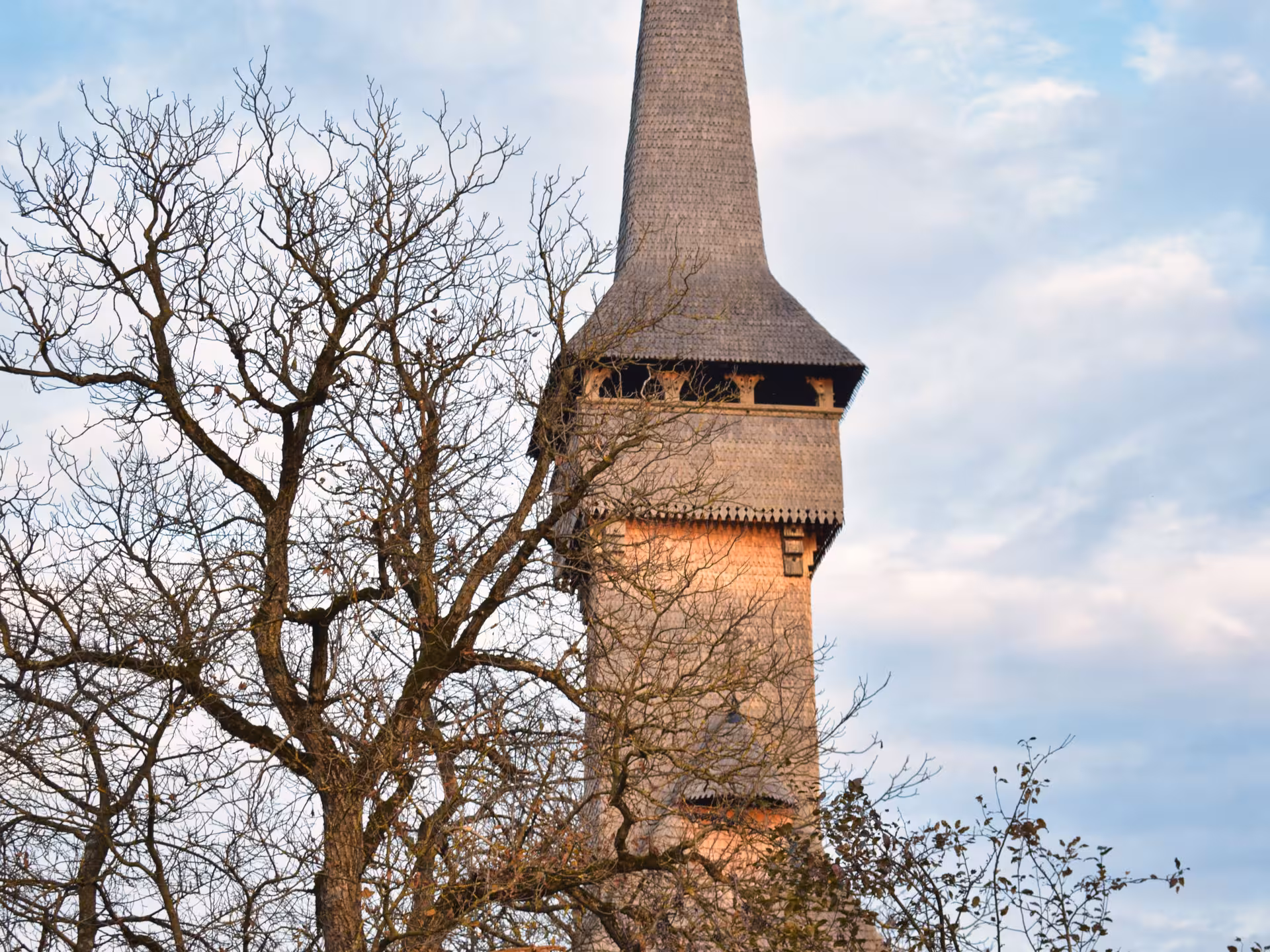 Iconic UNESCO wooden church tall spire rising above bare trees in Maramures on a guided tour from Cluj