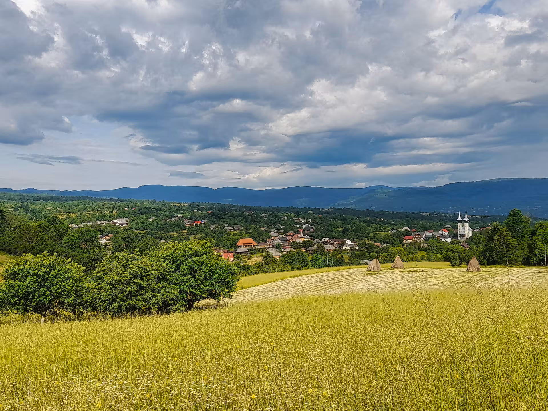 Panoramic view of Maramures village with haystacks, traditional church spires, and Carpathian mountains backdrop