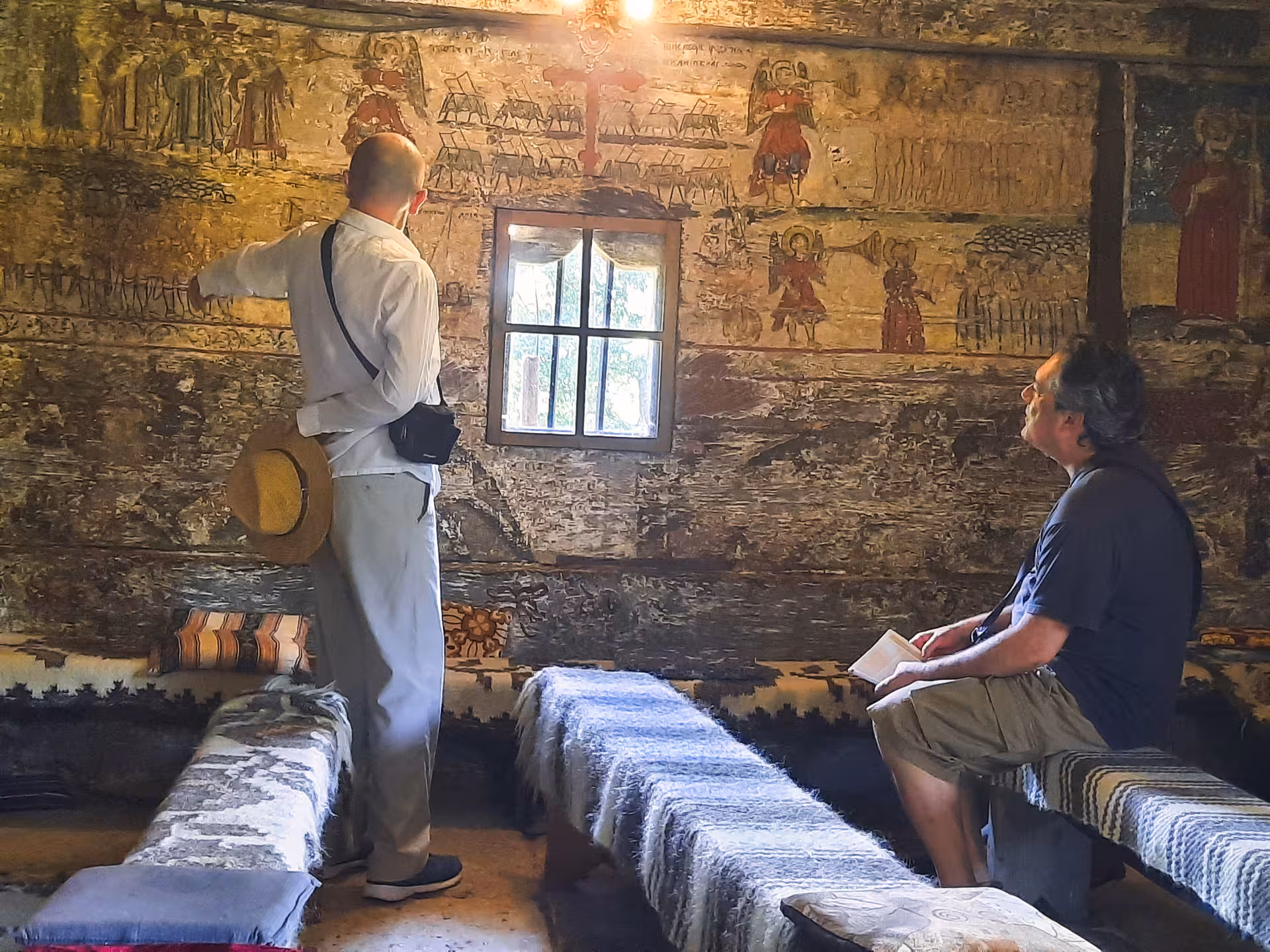 Tourists exploring ancient frescoes inside a traditional Maramures wooden church on a guided tour from Cluj Romania