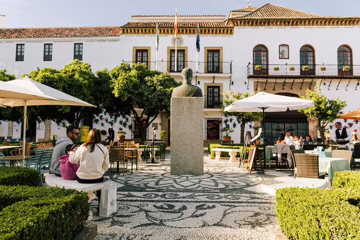 Charming Marbella Old Town square with a statue, outdoor cafes, and historic architecture for a local group tour experience.
