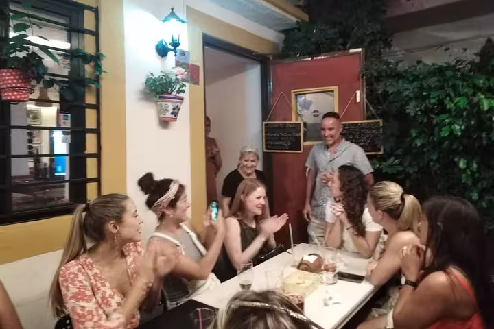 Group of excited tourists clapping at a vibrant tapas bar in Marbella during the tapas adventure tour.