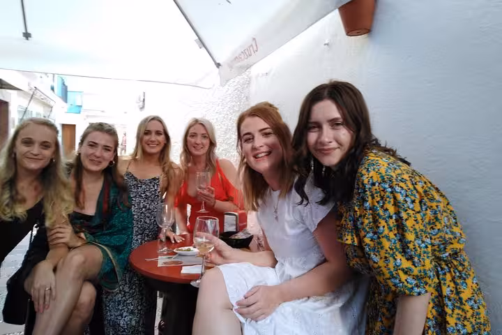 Smiling friends savoring wine and tapas in a charming Marbella outdoor cafe setting.