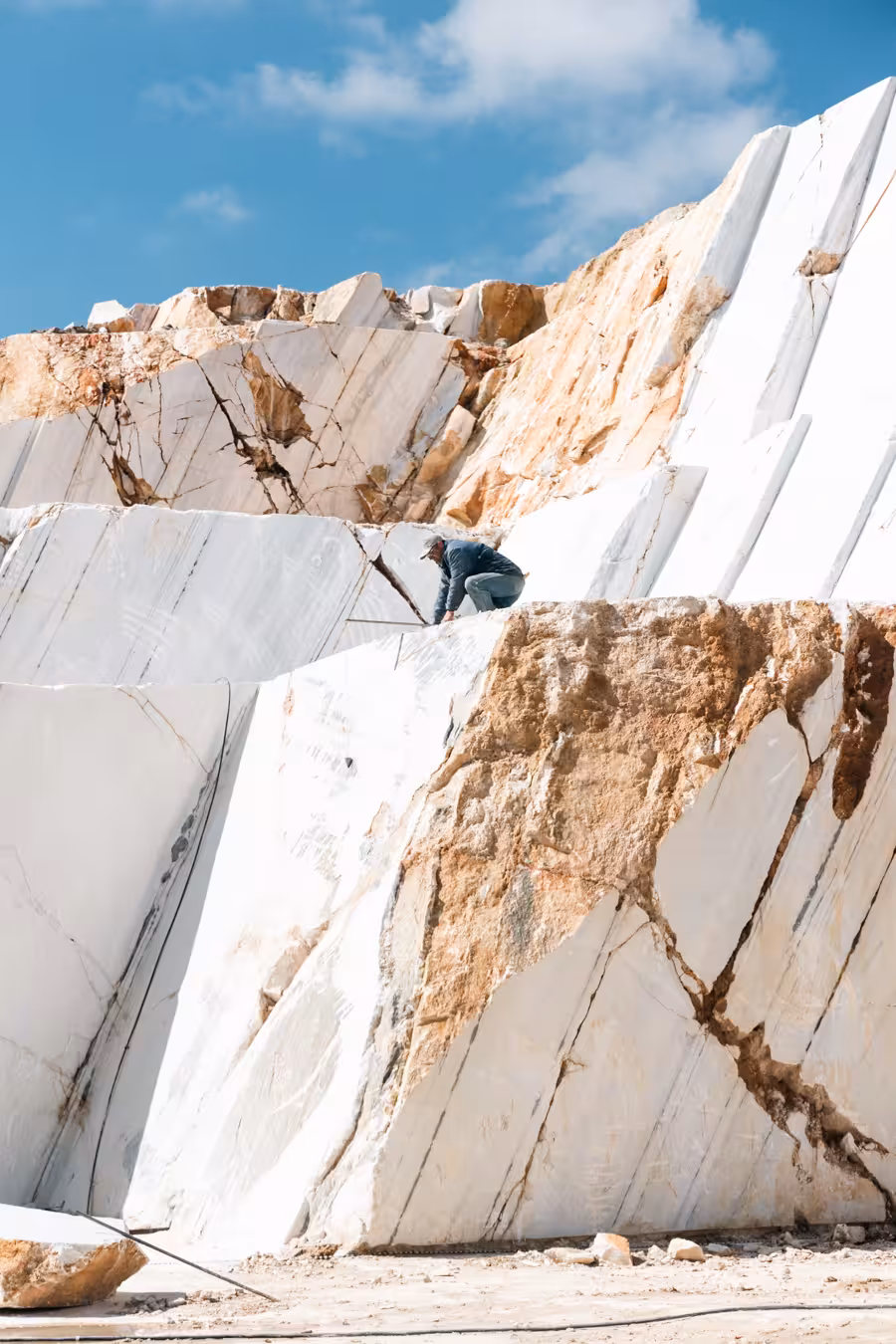 Marble World tour view of massive white marble quarry cliffs with a worker climbing under blue sky
