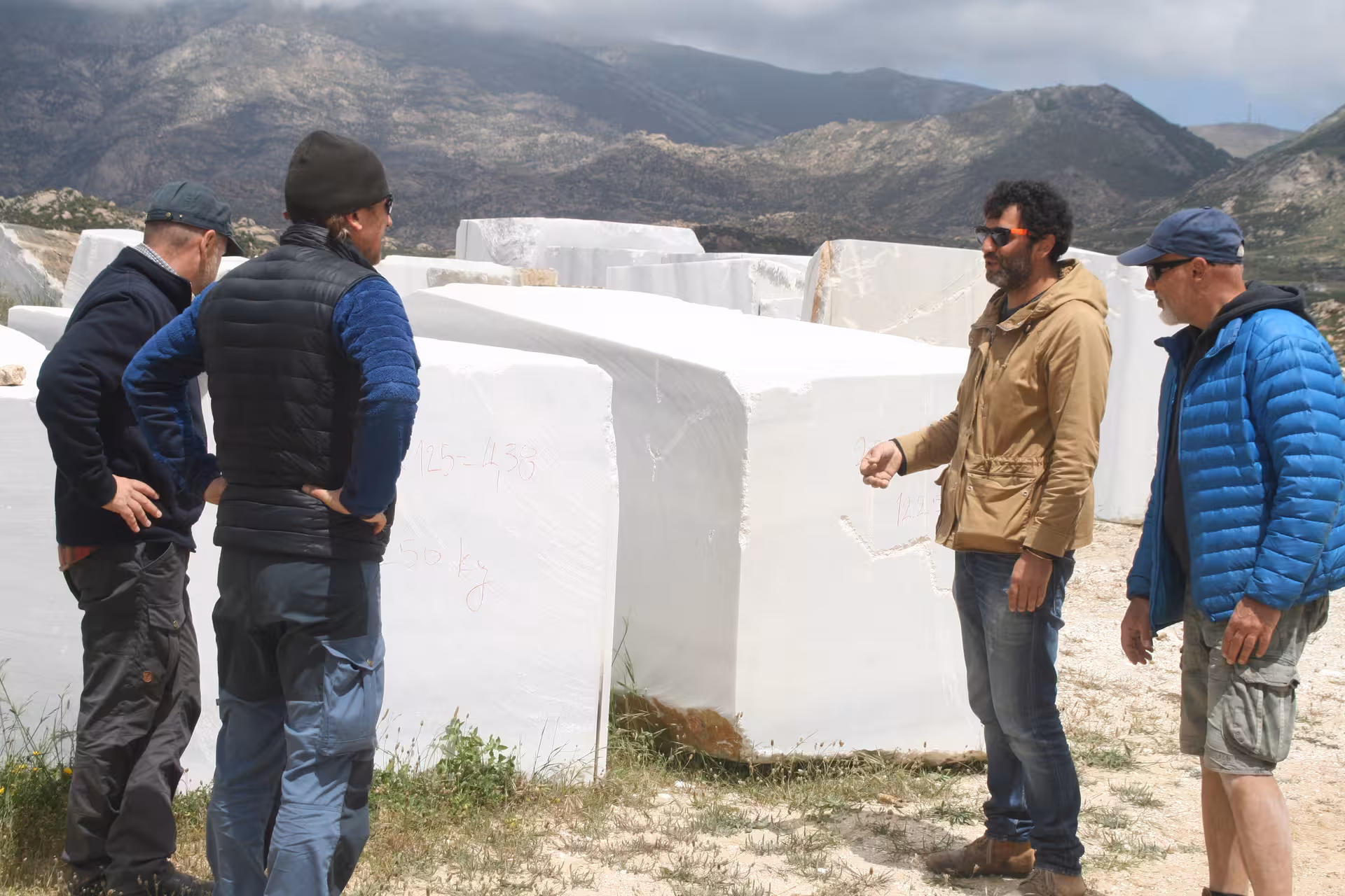 Marble World tour guide explaining massive white marble blocks in a quarry, with rugged mountains in the background