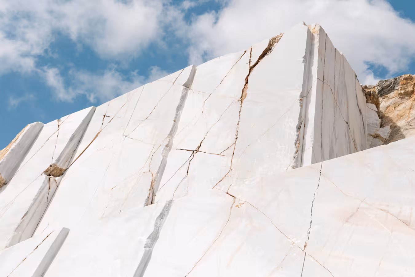 Towering white marble quarry face with natural veining under blue sky, highlight of the Marble World tour experience