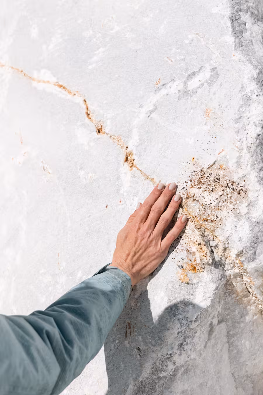 Close-up of hand touching veined white marble slab during Marble World tour, highlighting natural stone texture