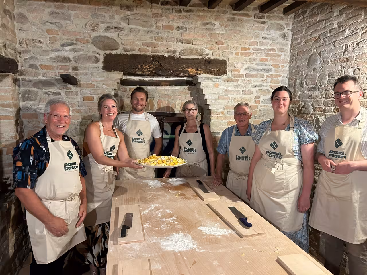 Group photo after Marche handmade pasta experience, guests in aprons holding fresh tagliatelle in a rustic stone kitchen