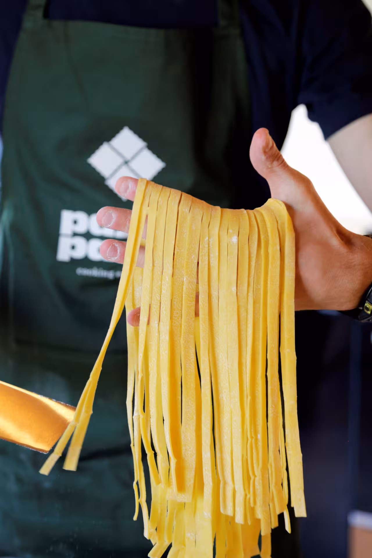 Fresh tagliatelle pasta strands held by a cook in an apron, part of a Marche make-your-own pasta workshop
