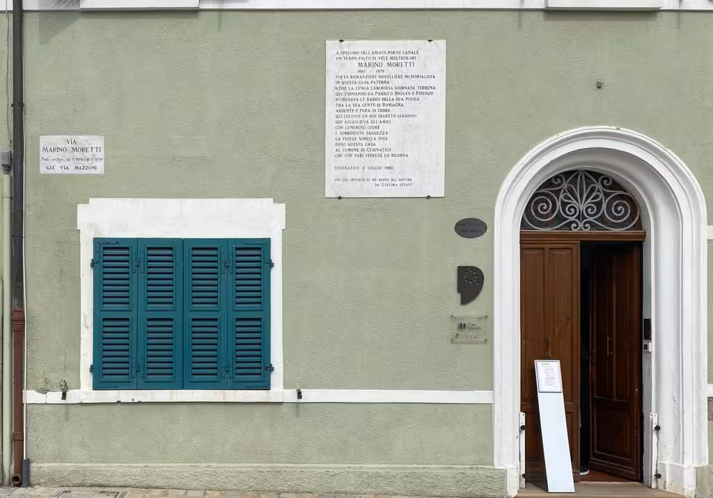 Entrance of Marino Moretti House museum in Cesenatico, Italy, with teal shutters and memorial plaque
