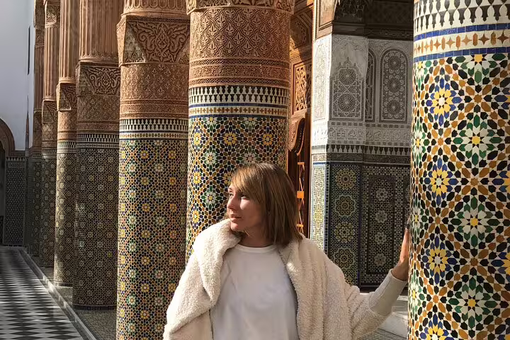 Traveler by colorful zellige columns in Marrakech medina palace, exploring Islamic mosaics on guided old city tour