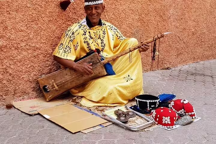 Marrakech street musician in traditional dress playing guembri in the old medina on guided city tour