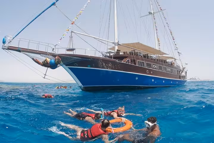 Snorkelers in the Red Sea beside Marsa Alam pirates sailing boat at Turtle Bay, guided cruise with hotel pickup