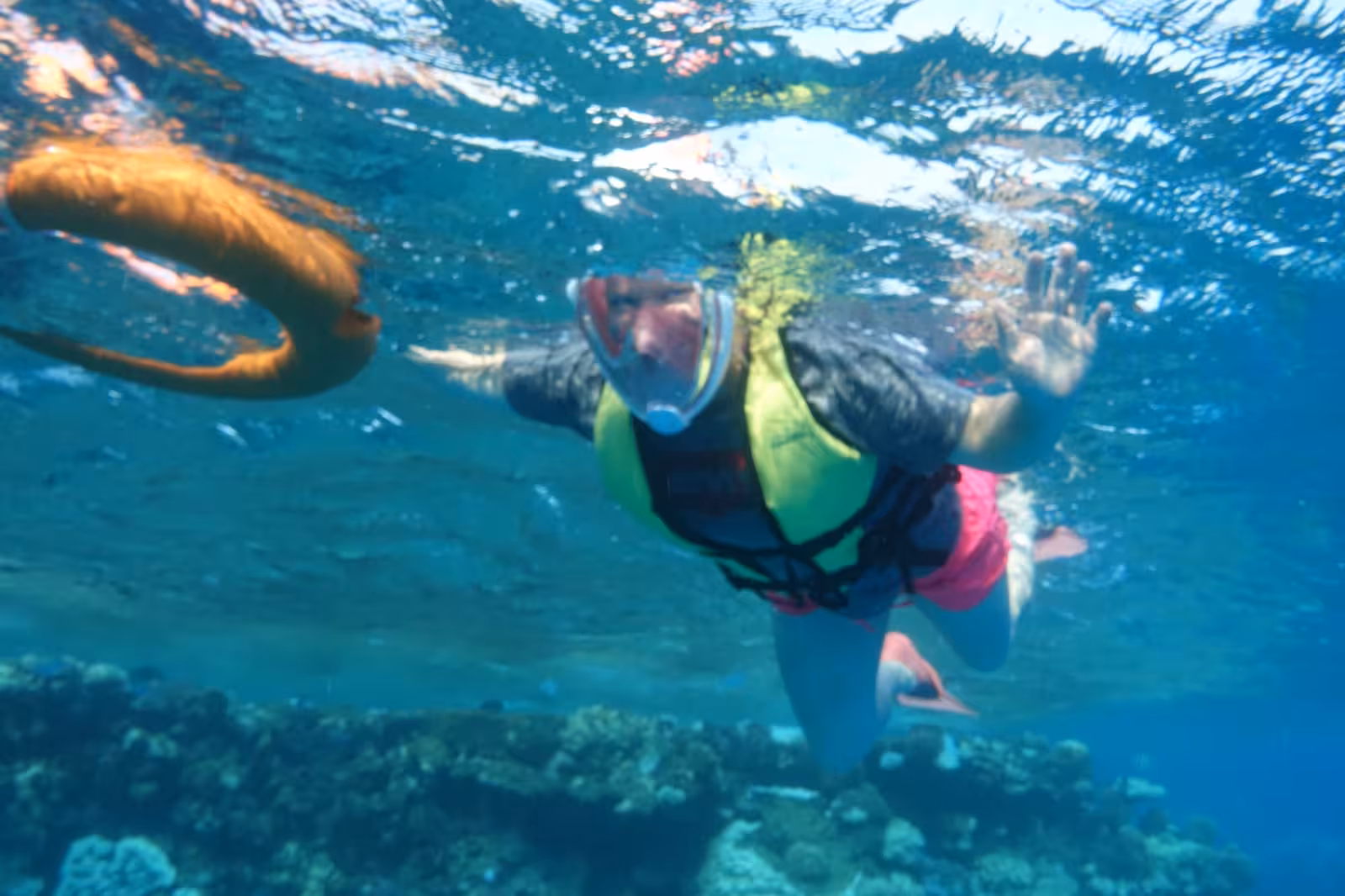 Snorkeler in full-face mask and life jacket underwater over coral reef in Marsa Alam
