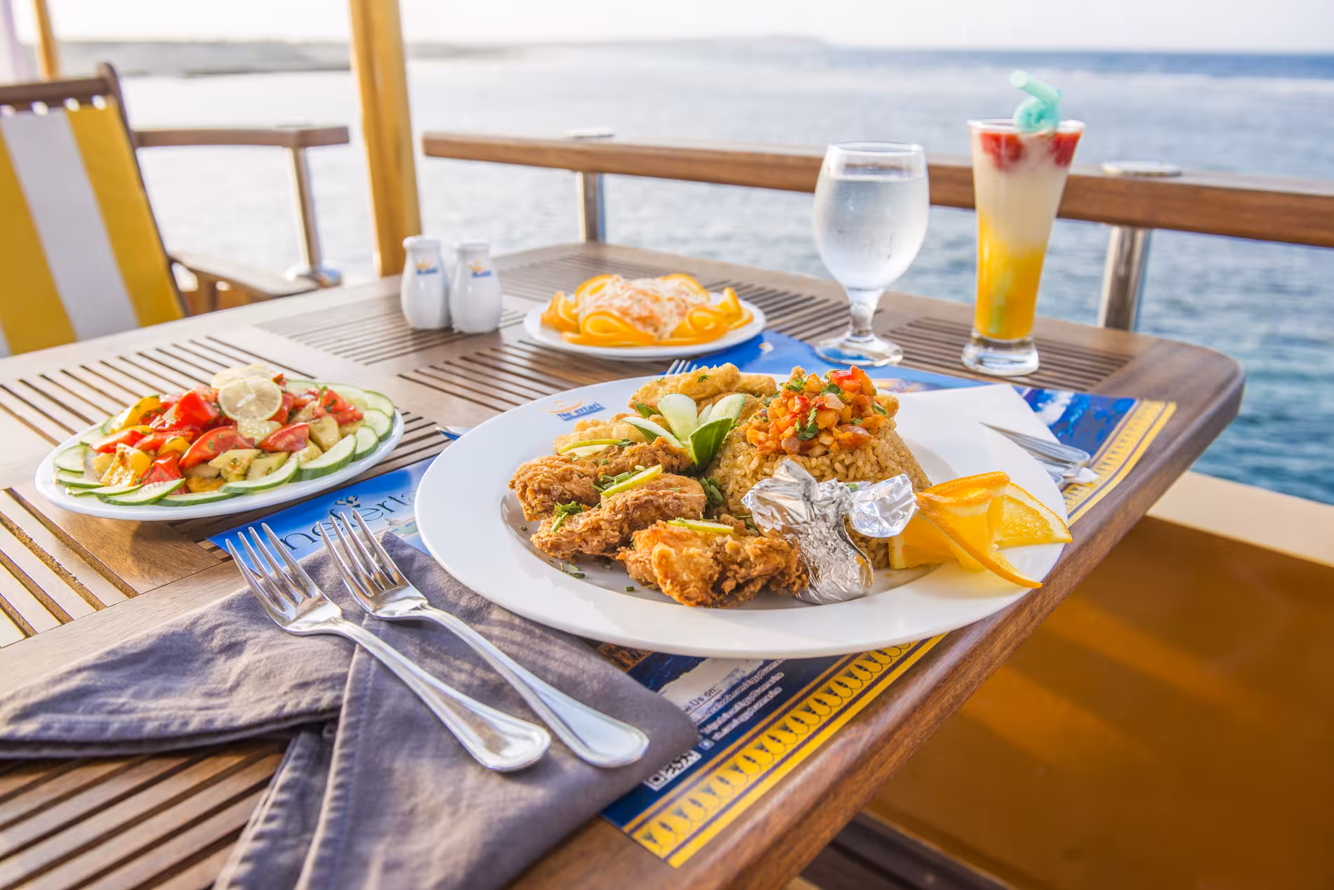 Fresh seafood meal with fried fish, rice, salad, and tropical drinks at a waterfront restaurant in Marsa Alam