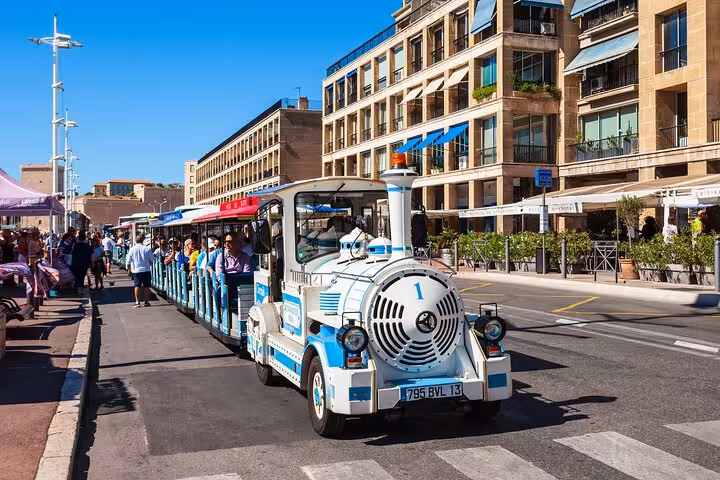 Tourists aboard a charming blue and white train exploring the vibrant streets of Marseille.