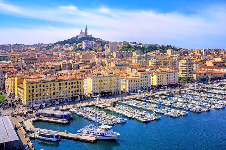 Aerial view of Marseille Old Port with boats, colorful buildings, and Notre-Dame de la Garde basilica on hill
