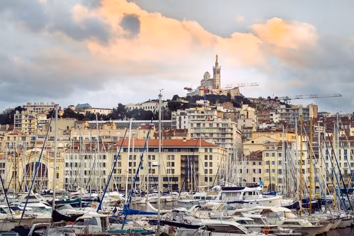 Marseille Old Port marina with sailboats and Notre-Dame de la Garde basilica on hilltop at sunset