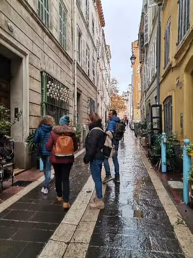 Travelers walking a rainy Marseille old town lane, exploring street art murals, local crafts and wine tasting