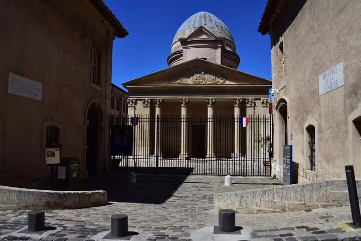 Neoclassical domed chapel with columns behind iron gates in Marseille Old Town cobblestone square