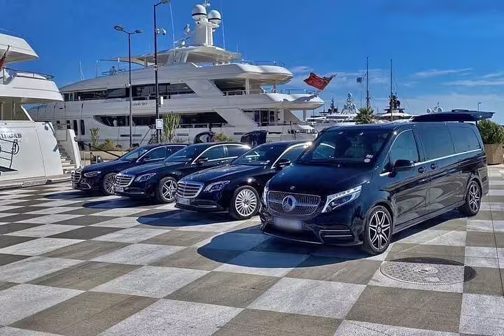 Fleet of black Mercedes luxury vehicles parked at marina with superyacht in background