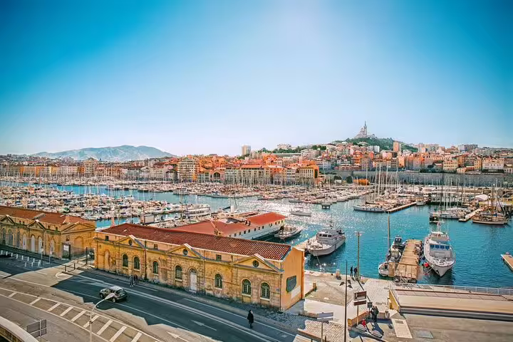 Aerial view of Marseille's Vieux-Port harbor with boats, colorful buildings, and Notre-Dame de la Garde basilica