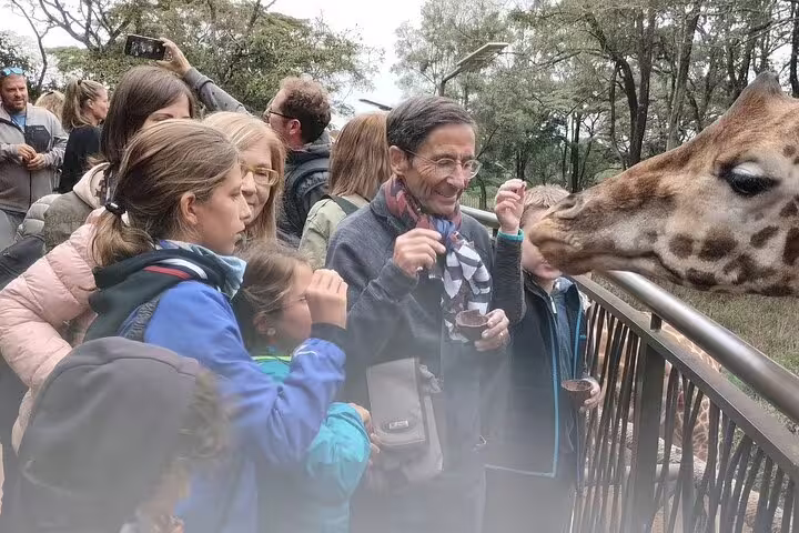 Tourists interact with a giraffe at an animal sanctuary, part of the 4-Day Masai Mara, Lake Naivasha Safari adventure.