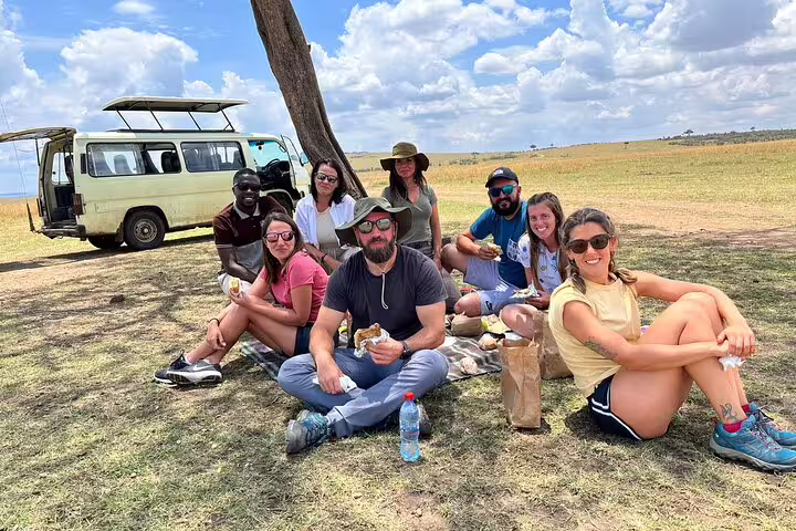 Group of tourists enjoying a picnic by a safari Jeep in Masai Mara, highlighting relaxation and adventure on a 3-day tour.