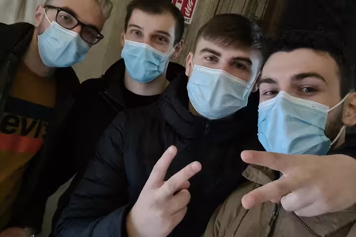 Four young men wearing blue surgical masks giving peace signs in a group selfie