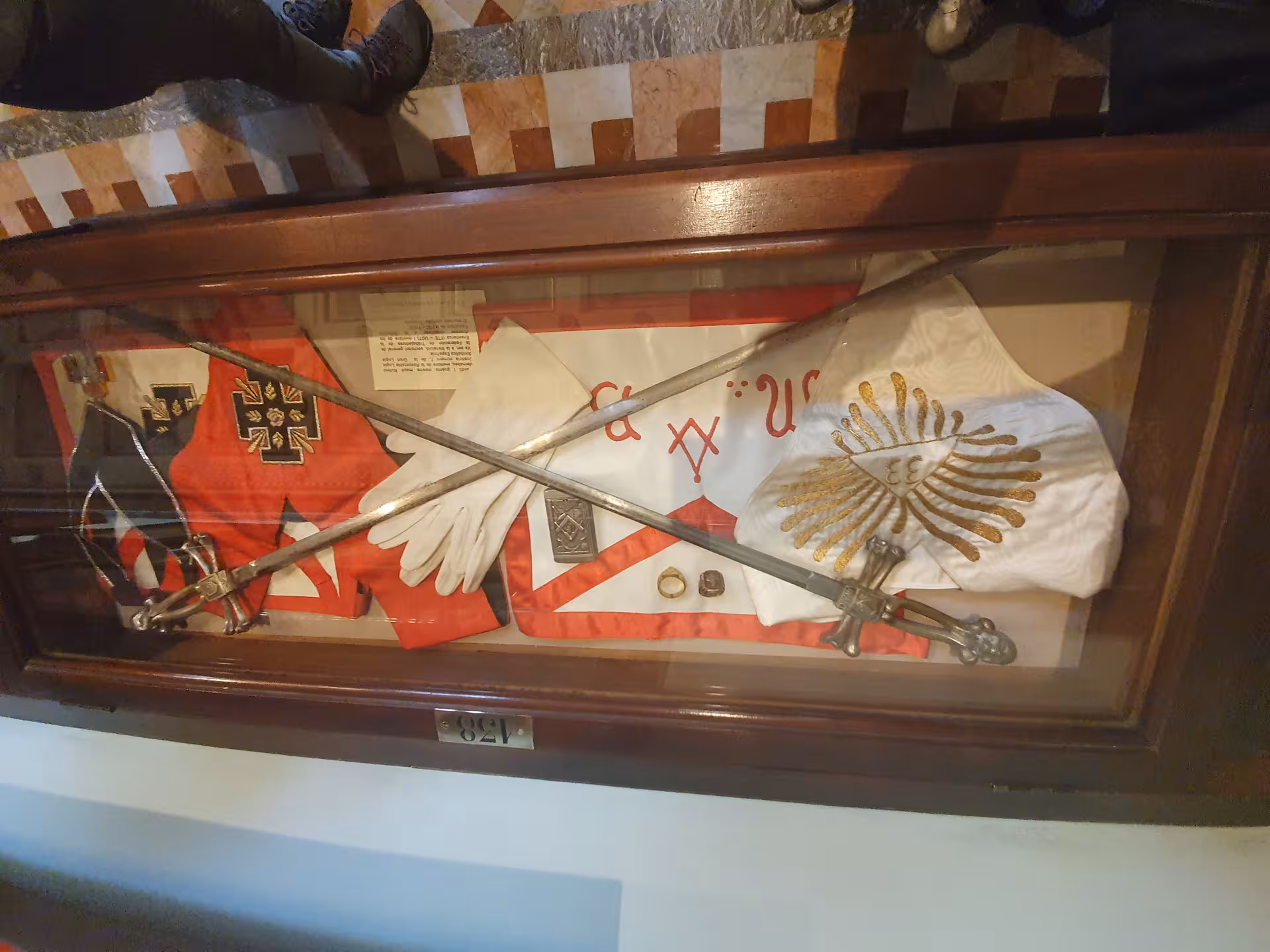 Explore Masonic heritage with ceremonial swords and regalia in a display case on the La Barcelona masónica tour.