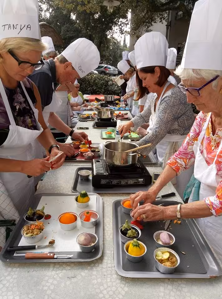 Guests in chef hats prepping Provençal dishes at an outdoor South of France master chef cooking workshop