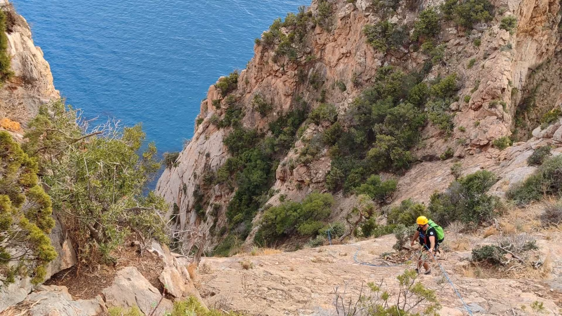 Climber navigates rugged terrain above Porto Flavia's blue waters, ideal for Masua dry canyoning experiences.