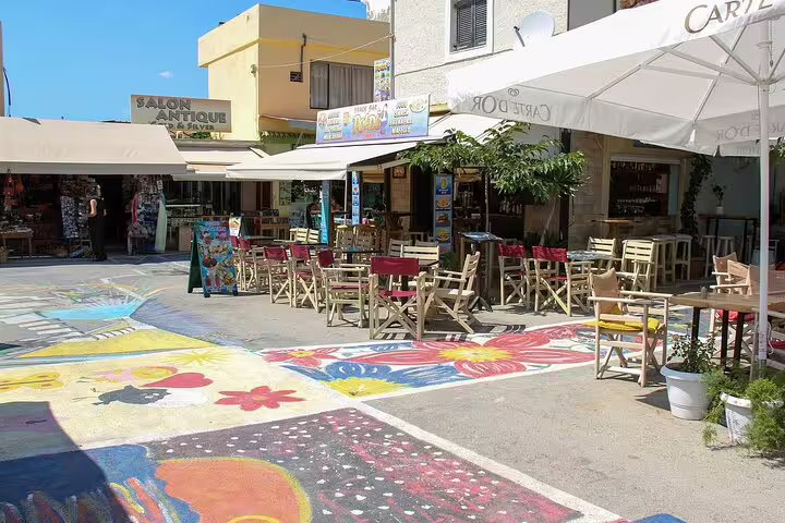 Colorful murals decorate a lively cafe-lined street in Matala, Crete, perfect for enjoying local cuisine and ambiance.