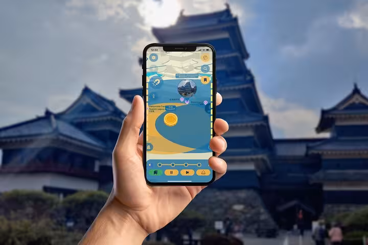 Hand holding smartphone with Matsumoto Castle self-guided tour app showing highlights of the iconic black Japanese castle