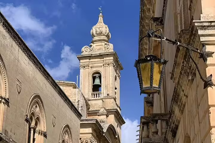 View of Mdina's historic architecture featuring a bell tower under a bright blue sky, perfect for Malta tours.