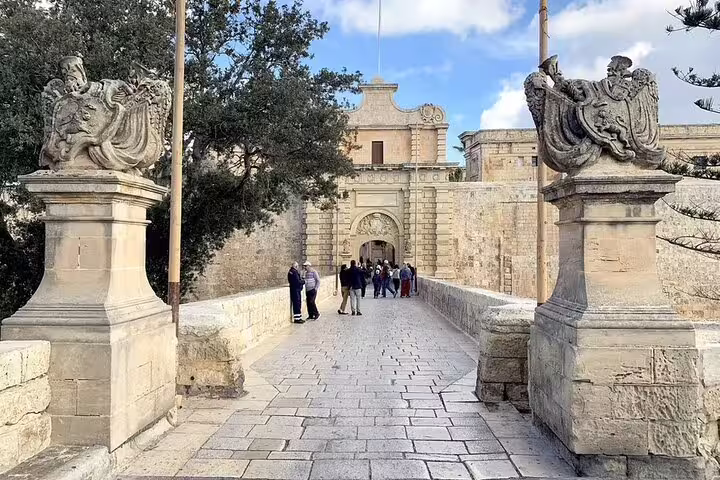 Tourists walking across the stone bridge leading to Mdina's grand entrance on a guided Malta tour.