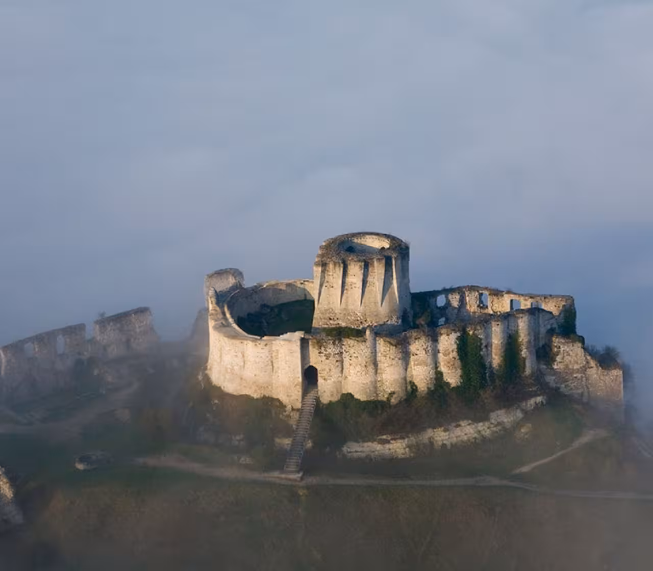 Aerial view of medieval castle ruins on a hilltop shrouded in morning mist, Normandy France