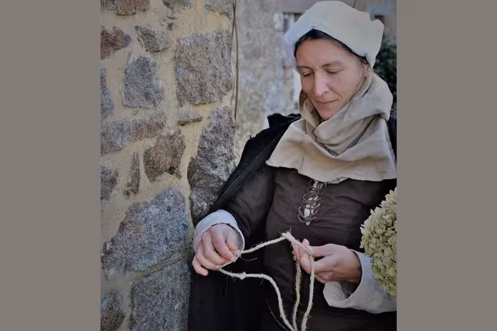 Woman in medieval costume spinning rope twine against stone wall in Dinan