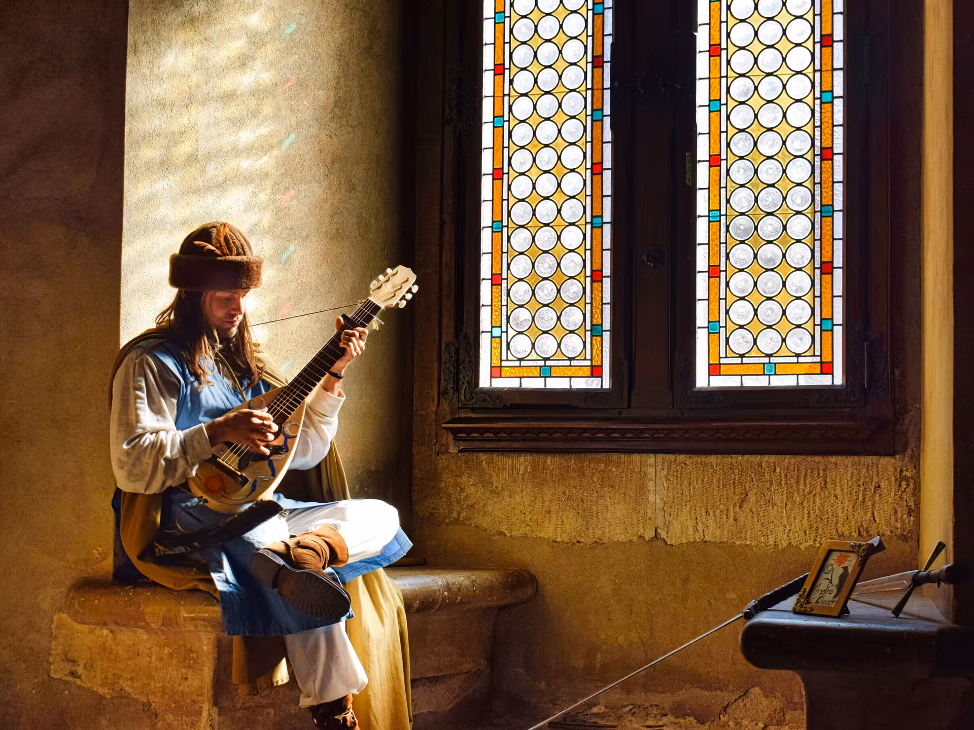 Medieval musician in costume playing lute inside Corvin Castle with colorful stained glass window backdrop