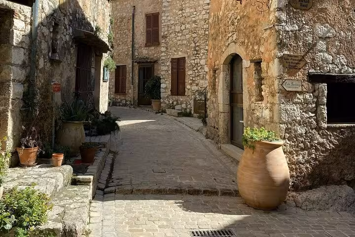 Sunlit cobblestone alley with rustic stone buildings and terracotta pots in a medieval Provence village