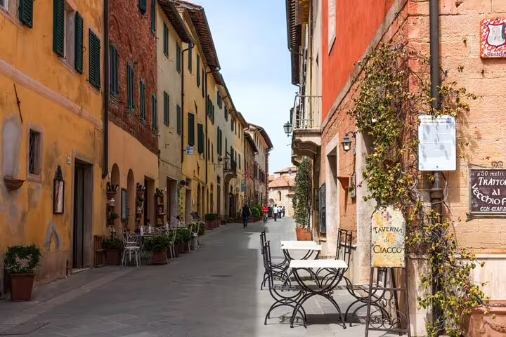 Narrow medieval street in Siena with colorful terracotta buildings, outdoor café tables, and Italian restaurant signs