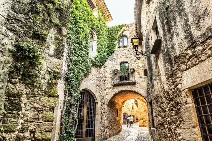 Charming cobblestone street with ivy-clad medieval stone buildings in a quaint Spanish village.