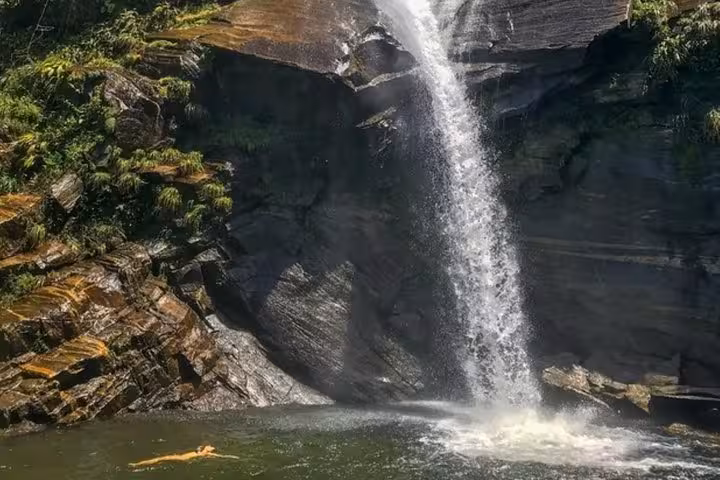 A serene view of Melancia Waterfall in Paraty, Brazil, with a person swimming in the clear pool below.