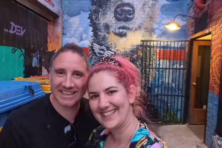 Couple smiling in Melbourne laneway with colorful street art mural on brick wall behind them