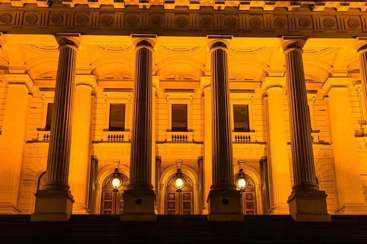 Melbourne neoclassical building facade illuminated in golden orange light at night with tall columns and arched doorways
