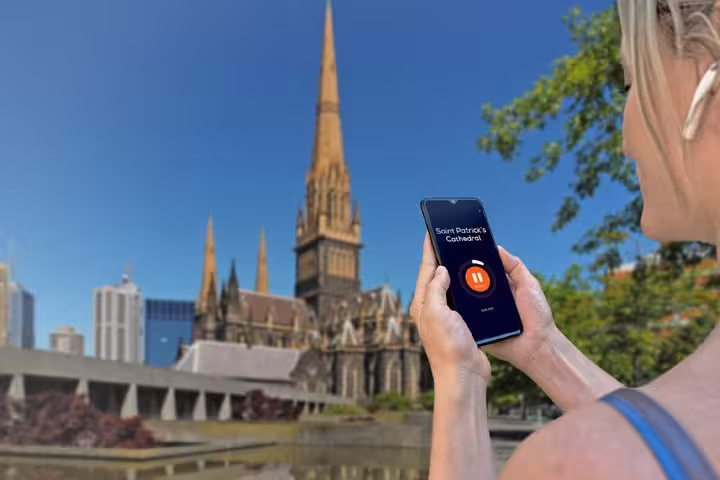 Tourist using audio tour app on smartphone with Saint Patrick's Cathedral Melbourne in background