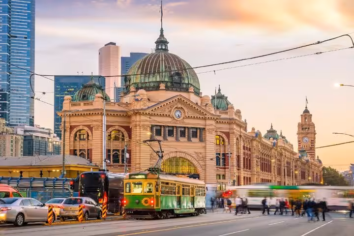 Green tram passing Flinders Street Station in Melbourne at dusk with bustling pedestrians